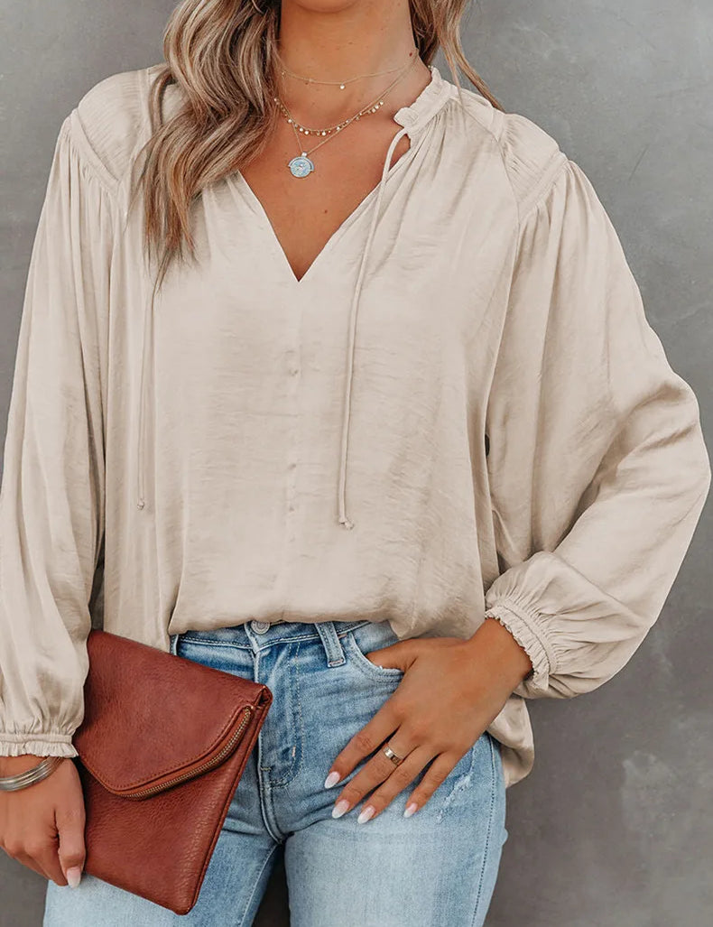 Mujer vistiendo una blusa beige de manga larga con diseño fluido, combinada con jeans de cintura alta y un bolso de mano marrón